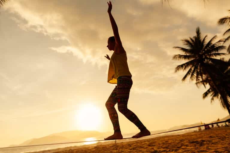 adolescente equilibrando-se no slackline na praia ao nascer do sol